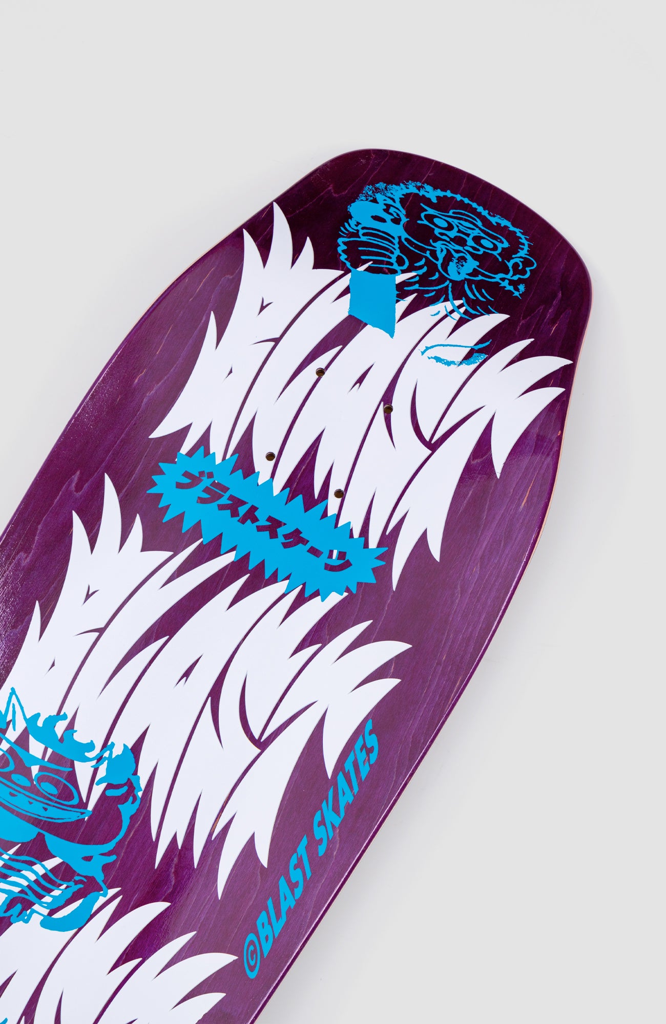 nahaufnahme von einem breiten skateboard deck mit lila gefärbtem holz und weißer Schrift als Aufdruck. das design erinnert an japanische Charaktere und Schrift.